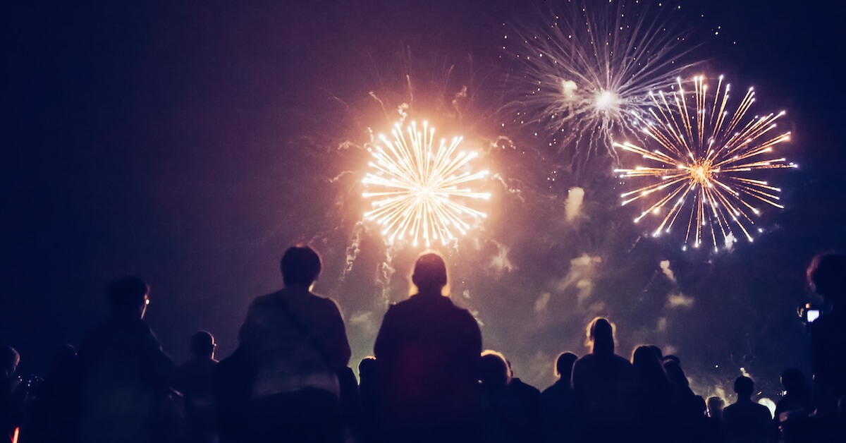 A crowd of people watches New Year's Eve fireworks.